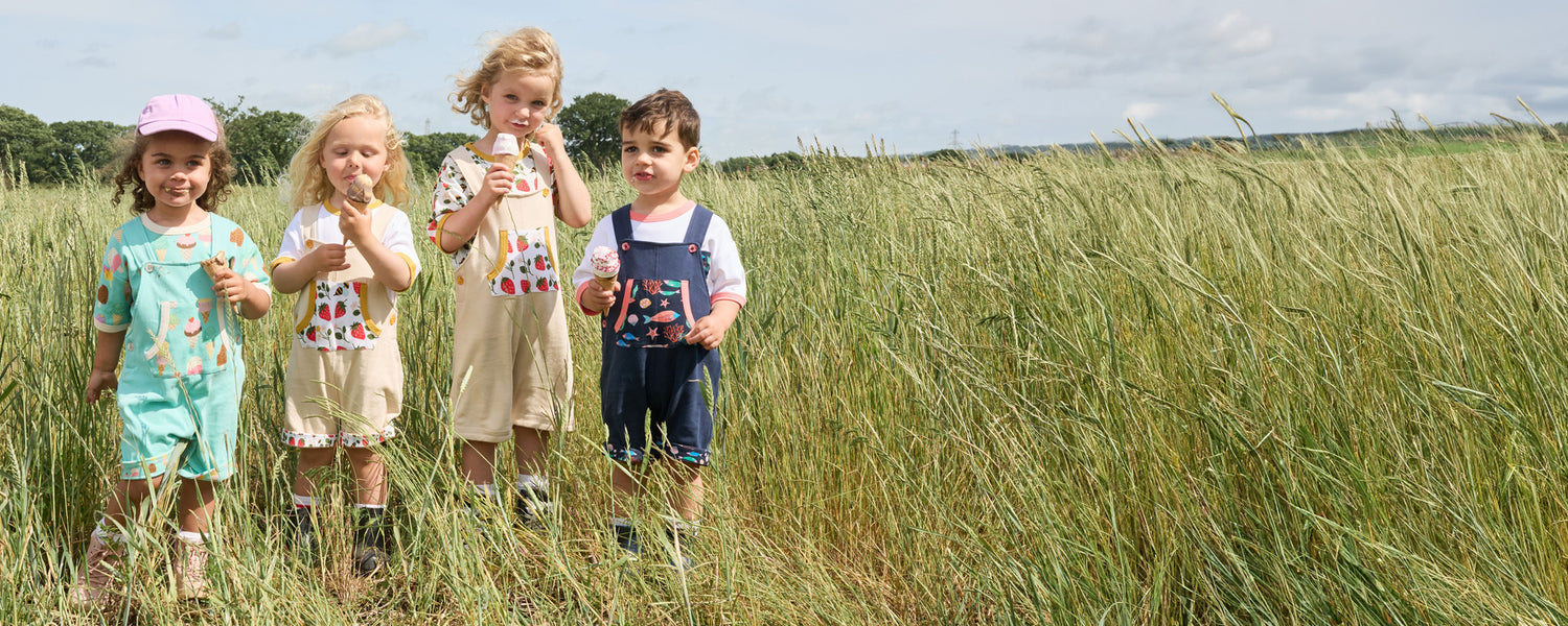 Group of children eating ice-cream I a field. They are wearing a selection of Playtime Prints outfits including strawberry, fish and ice cream prints.