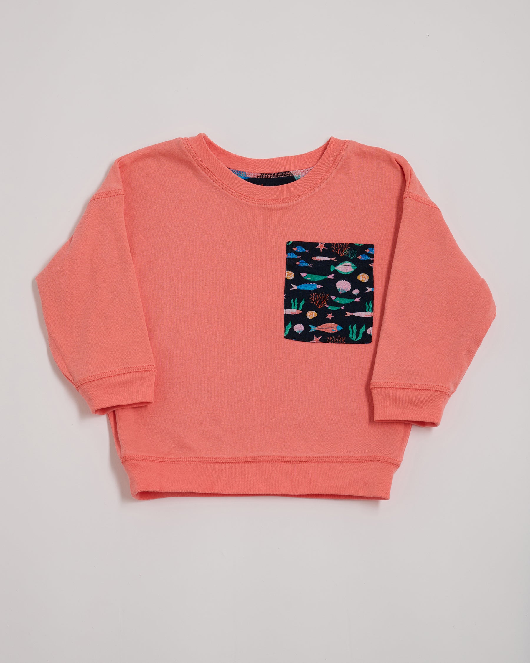 Front of coral sweatshirt with oversized vibrant navy fish print chest pocket.