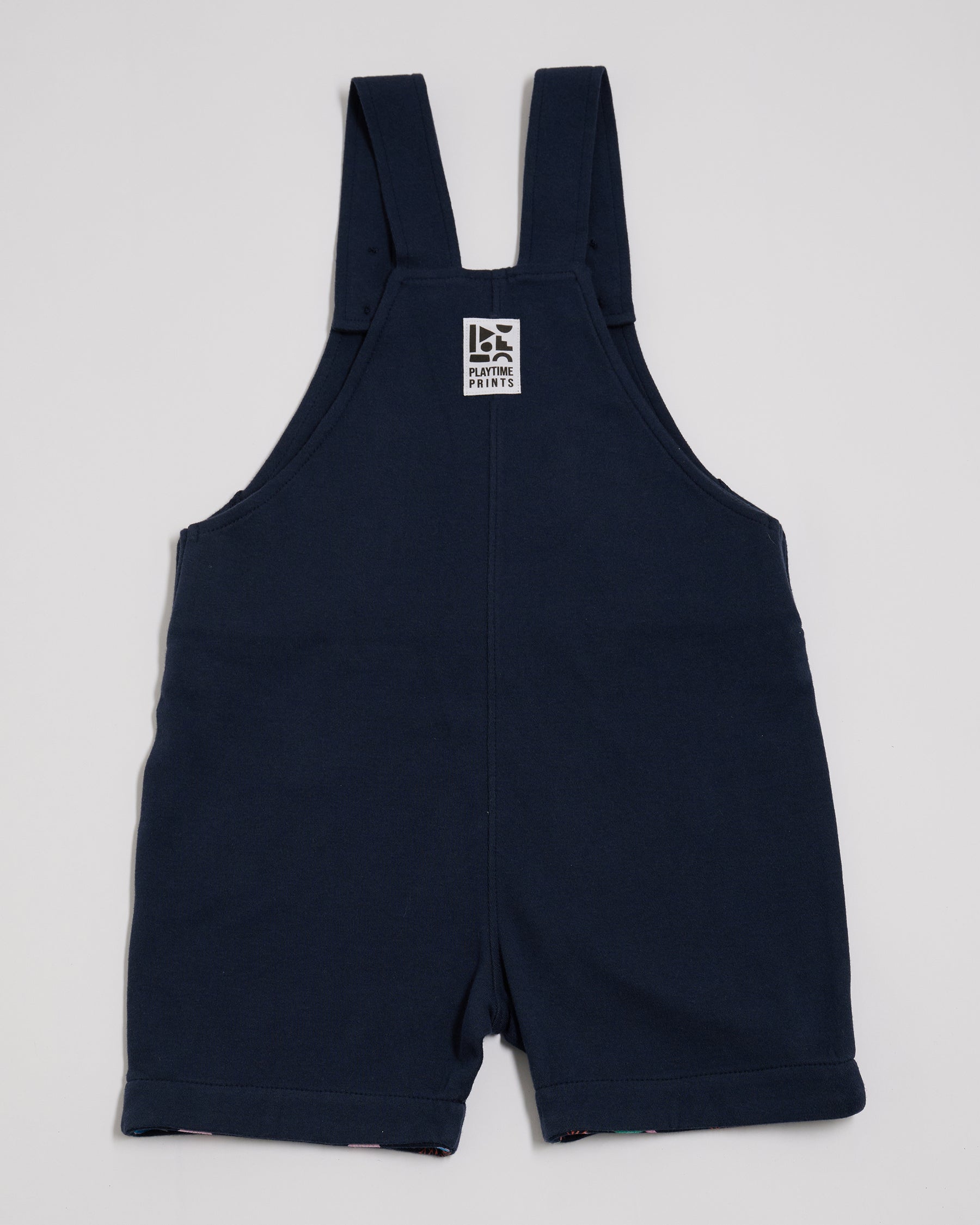 Back of navy short dungarees with Playtime Prints brand label.