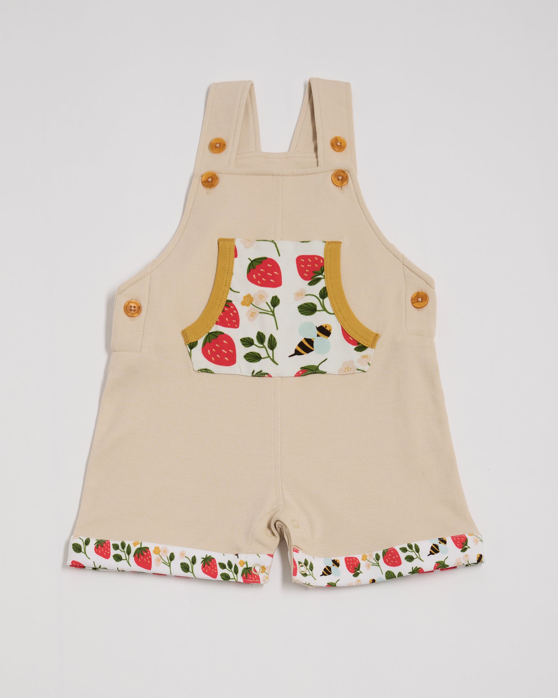 Front of beige short dungarees with fun strawberry and bees print pocket and fixed turn-ups, adjustable straps, crotch poppers, honey buttons and honey trim.