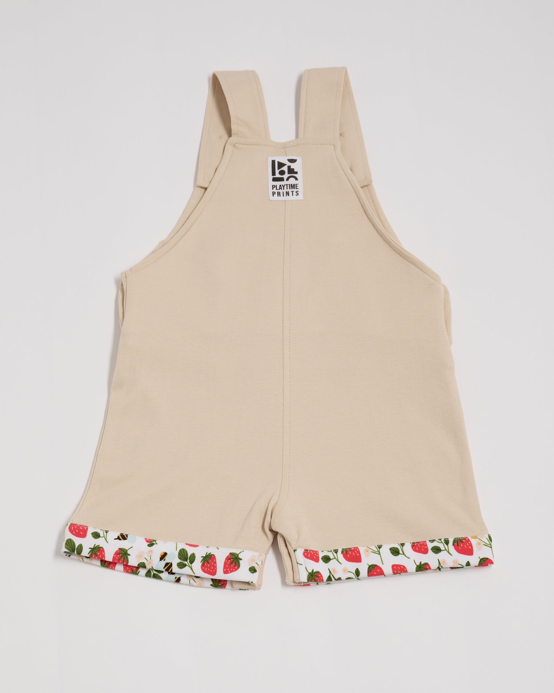 Back of beige short dungarees with fun strawberry and bee print fixed turn-ups and Playtime Prints brand label.