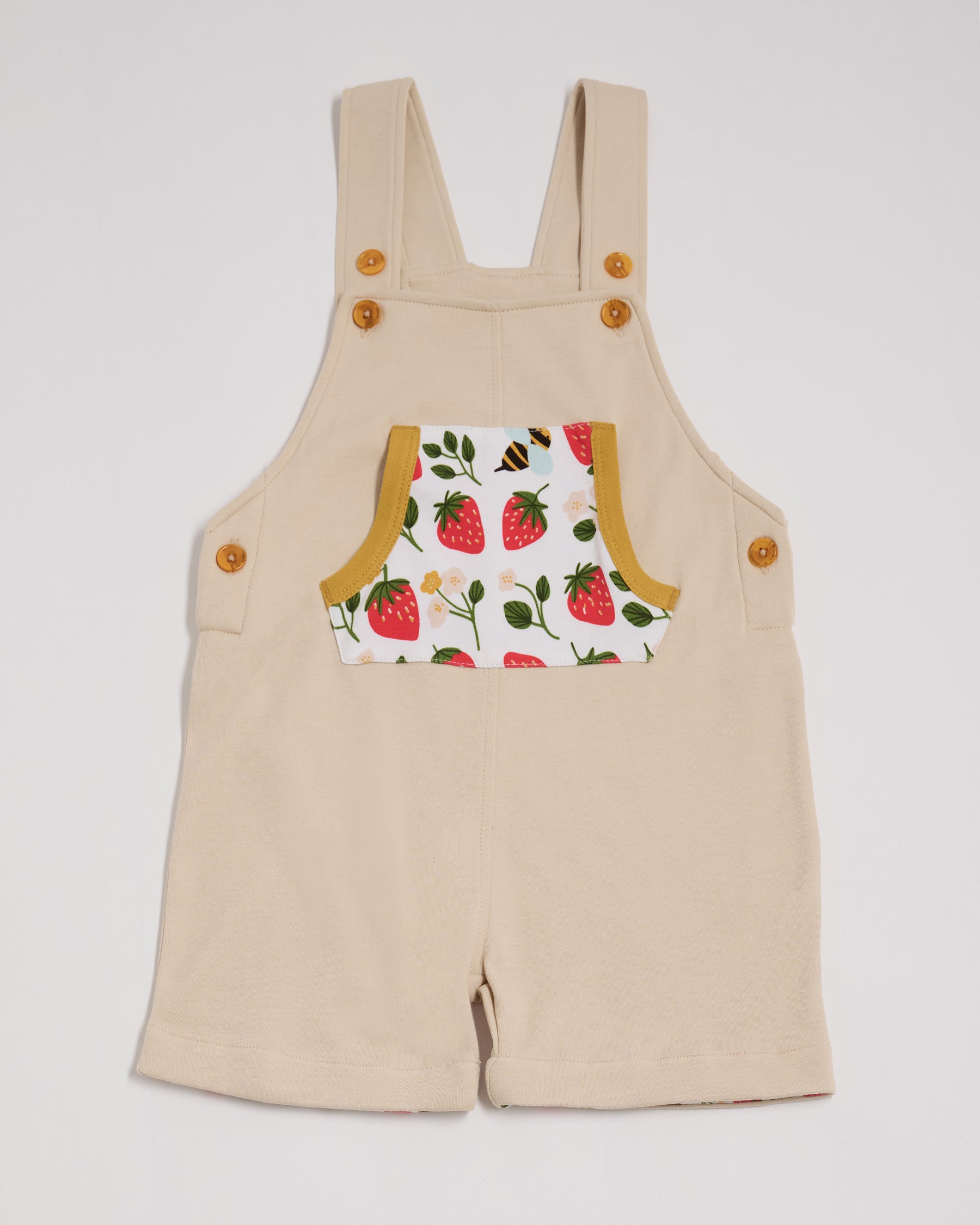 Front view of beige dungarees with fun strawberry and bees print pocket, adjustable straps, honey buttons and honey trim.