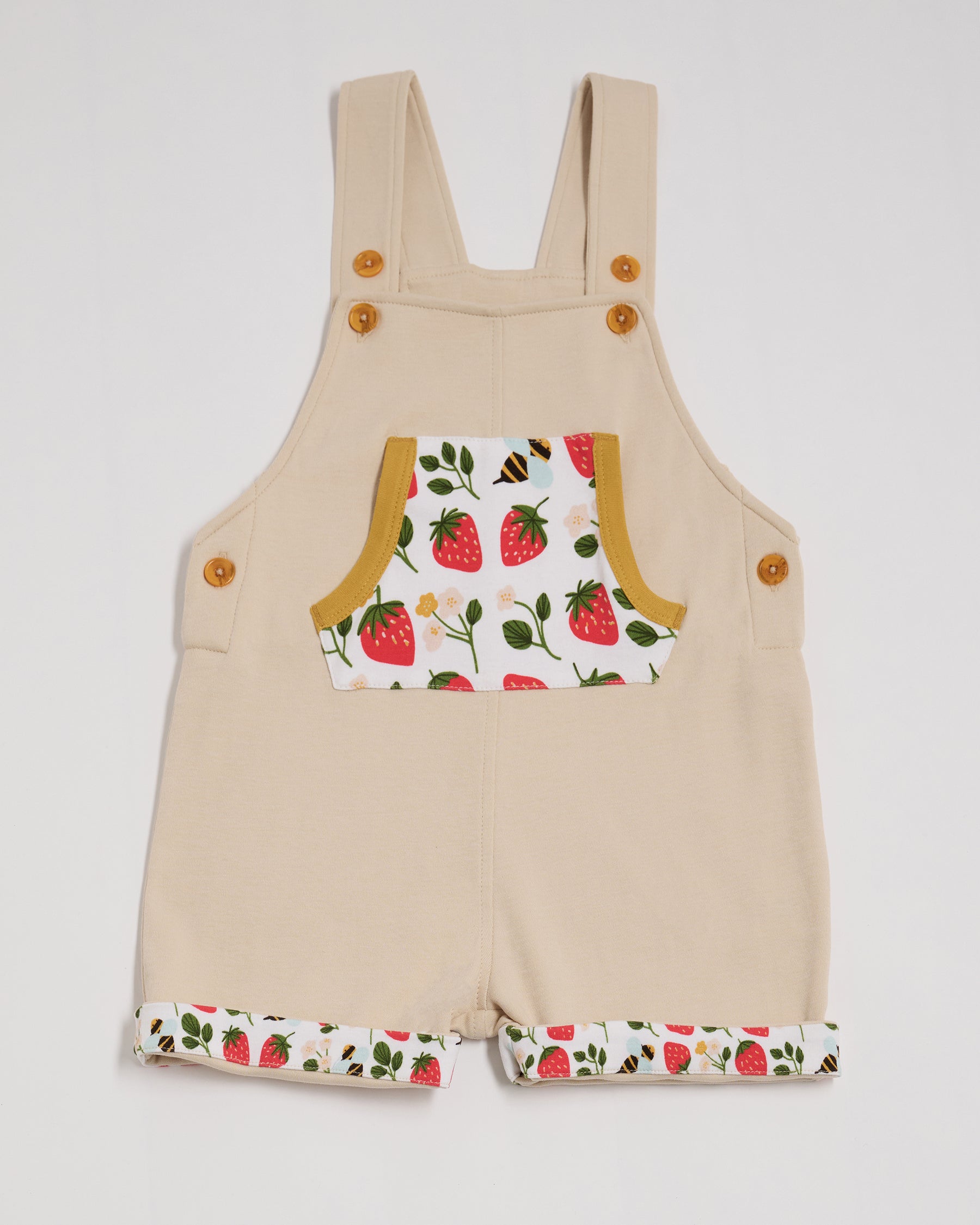 Front of beige short dungarees with fun strawberry and bees print pocket and turn-ups, adjustable straps, honey buttons and honey trim.