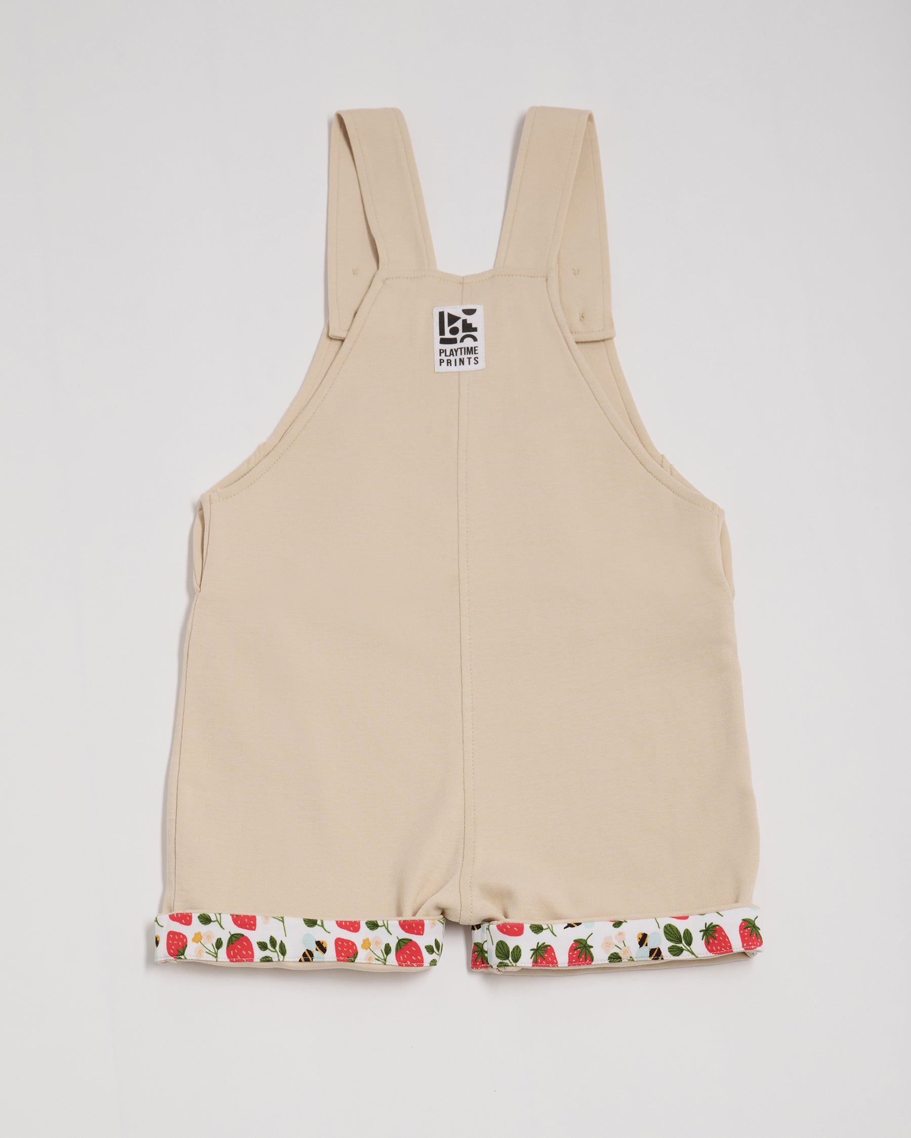 Back of beige short dungarees with fun strawberry and bees print turn-ups and Playtime Prints brand label.