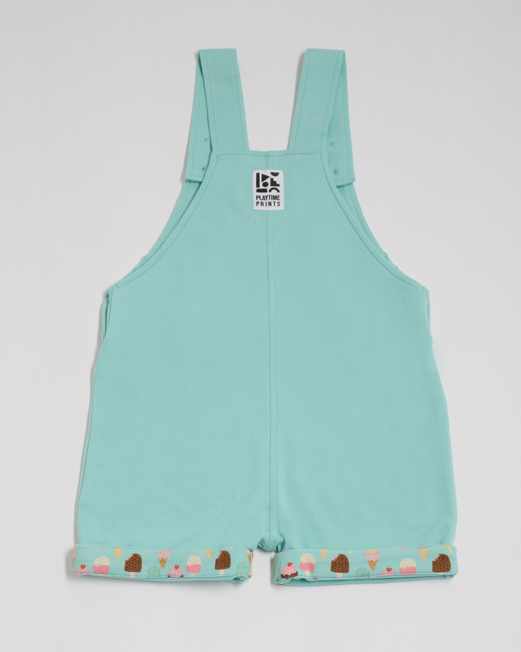Back of short turquoise dungarees with bright ice cream print turn-ups and Playtime Prints brand label.