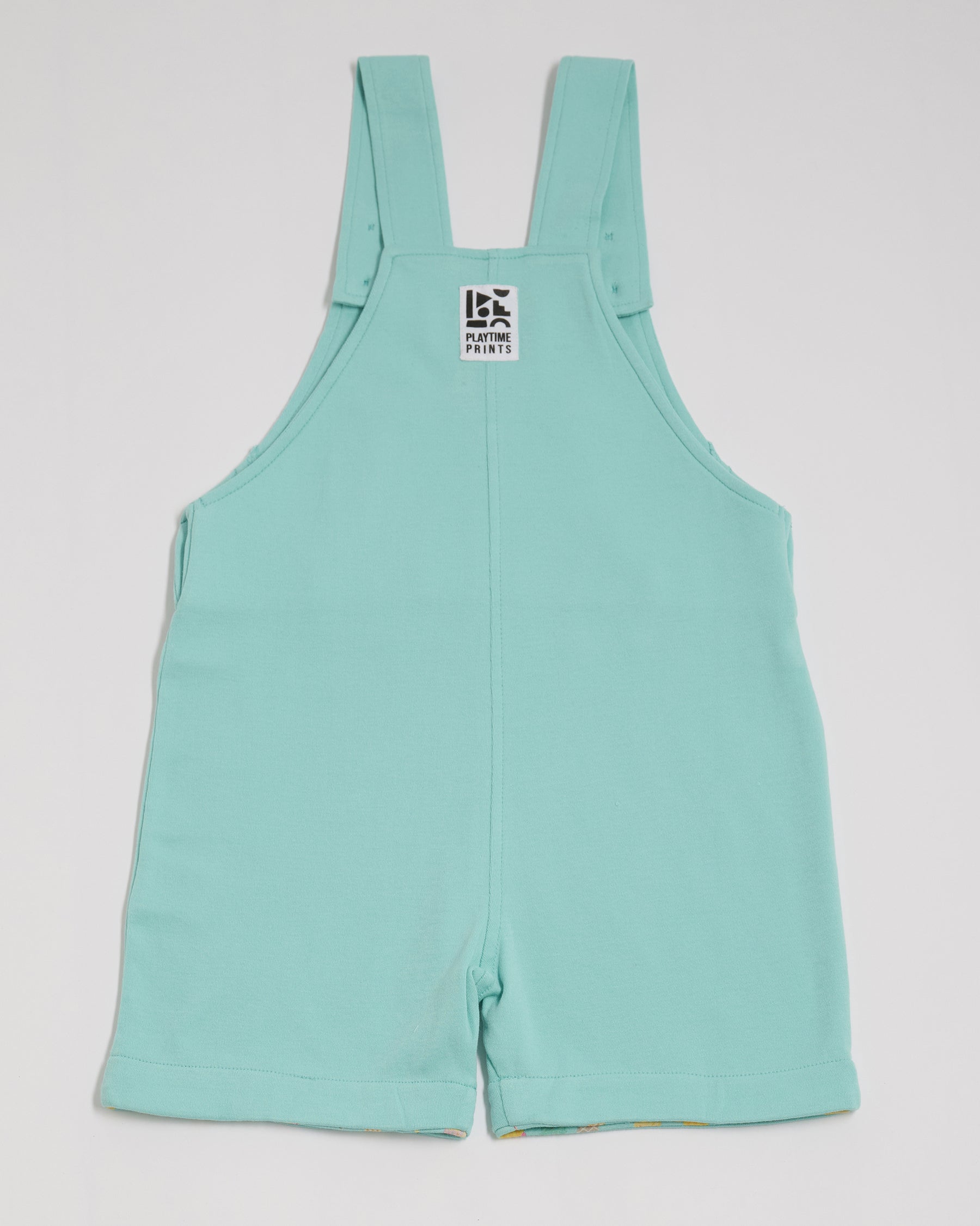 Back of turquoise short dungarees with Playtime Prints brand label.