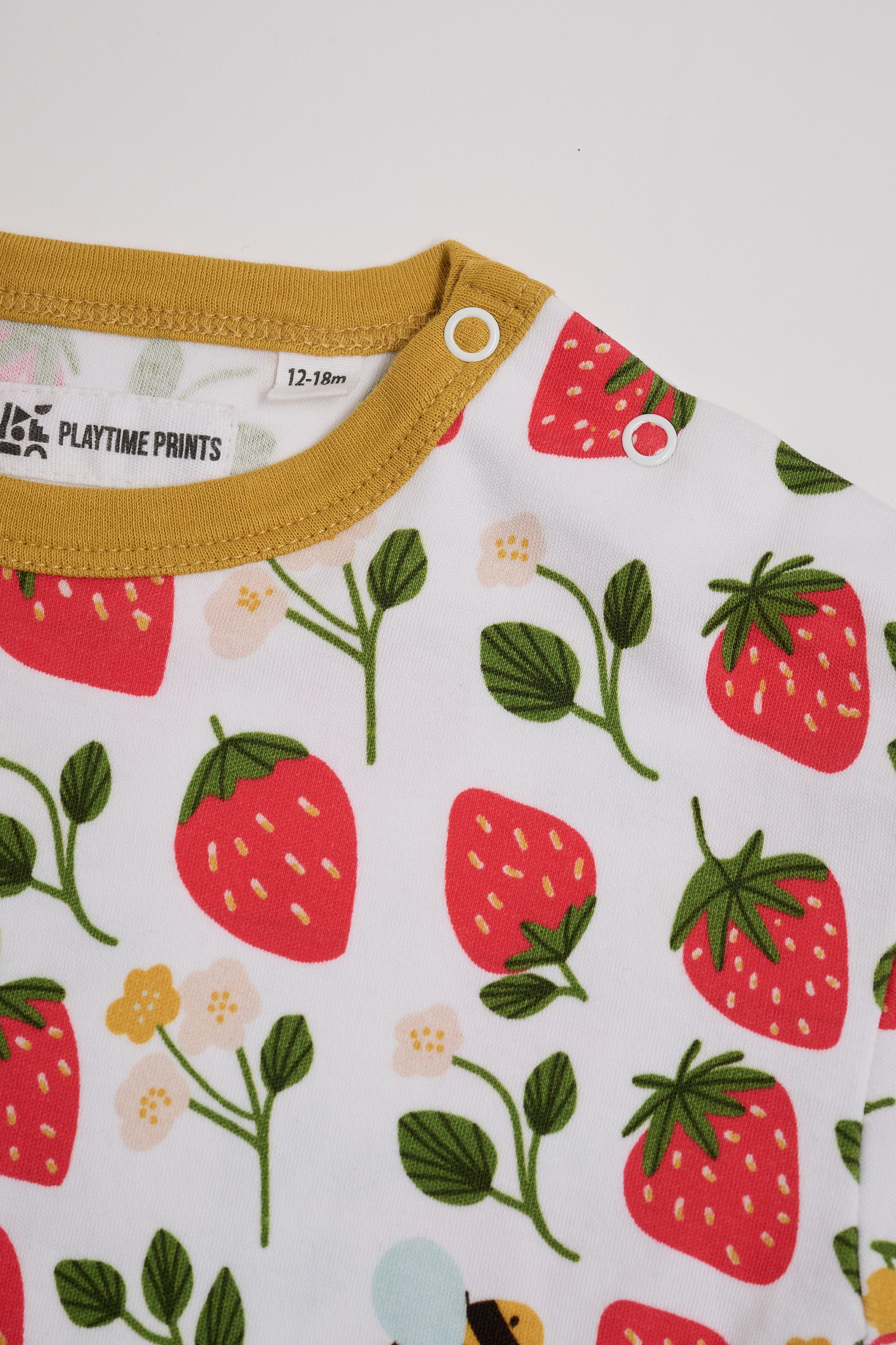 Close-up of neck poppers on a short sleeved t-shirt featuring an all over strawberry and bees print with contrast honey neck and sleeve trim.