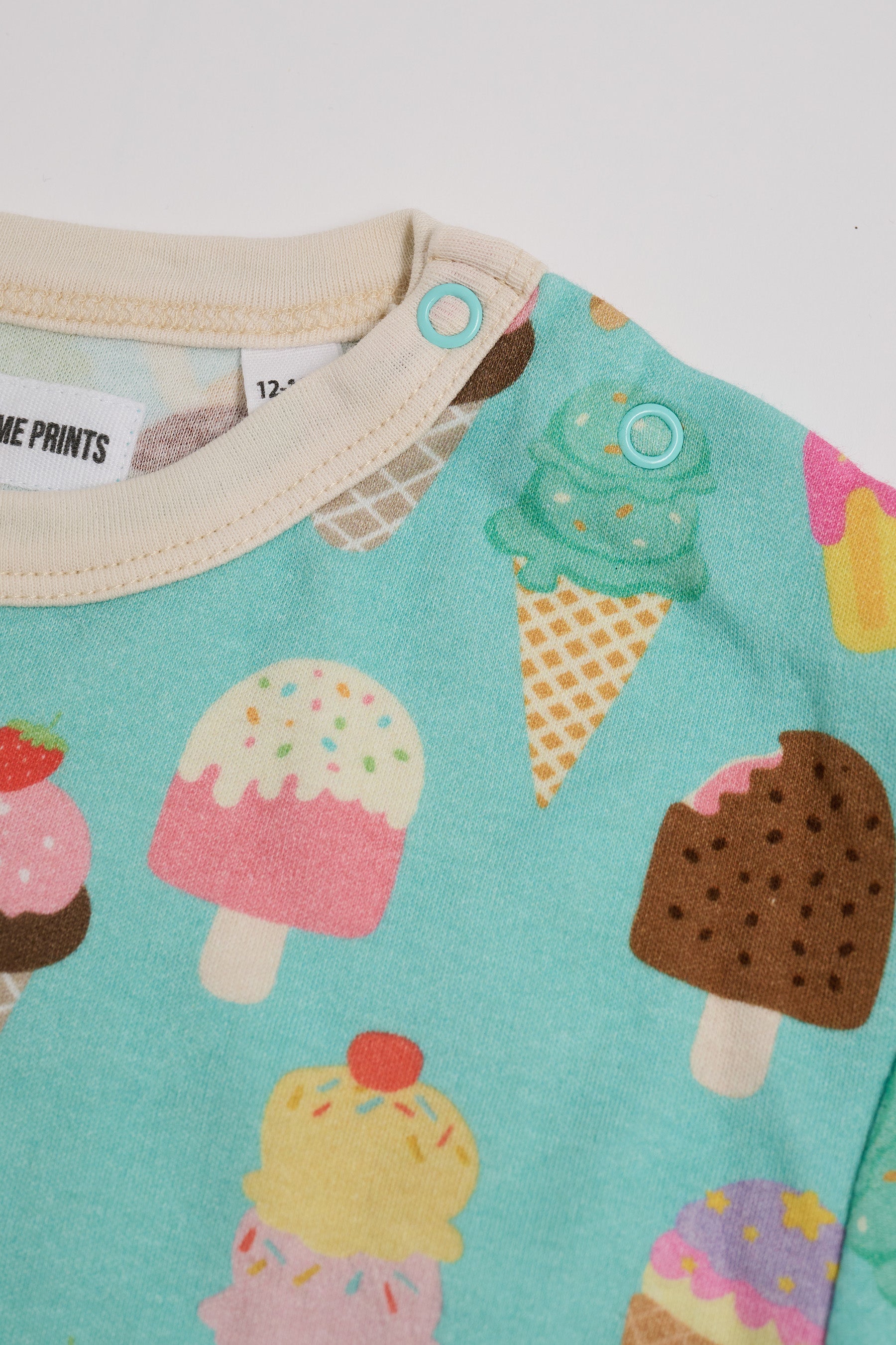 Close-up of neck poppers on a short sleeved t-shirt featuring an all over turquoise ice cream print with contrast ecru neck and sleeve trim.