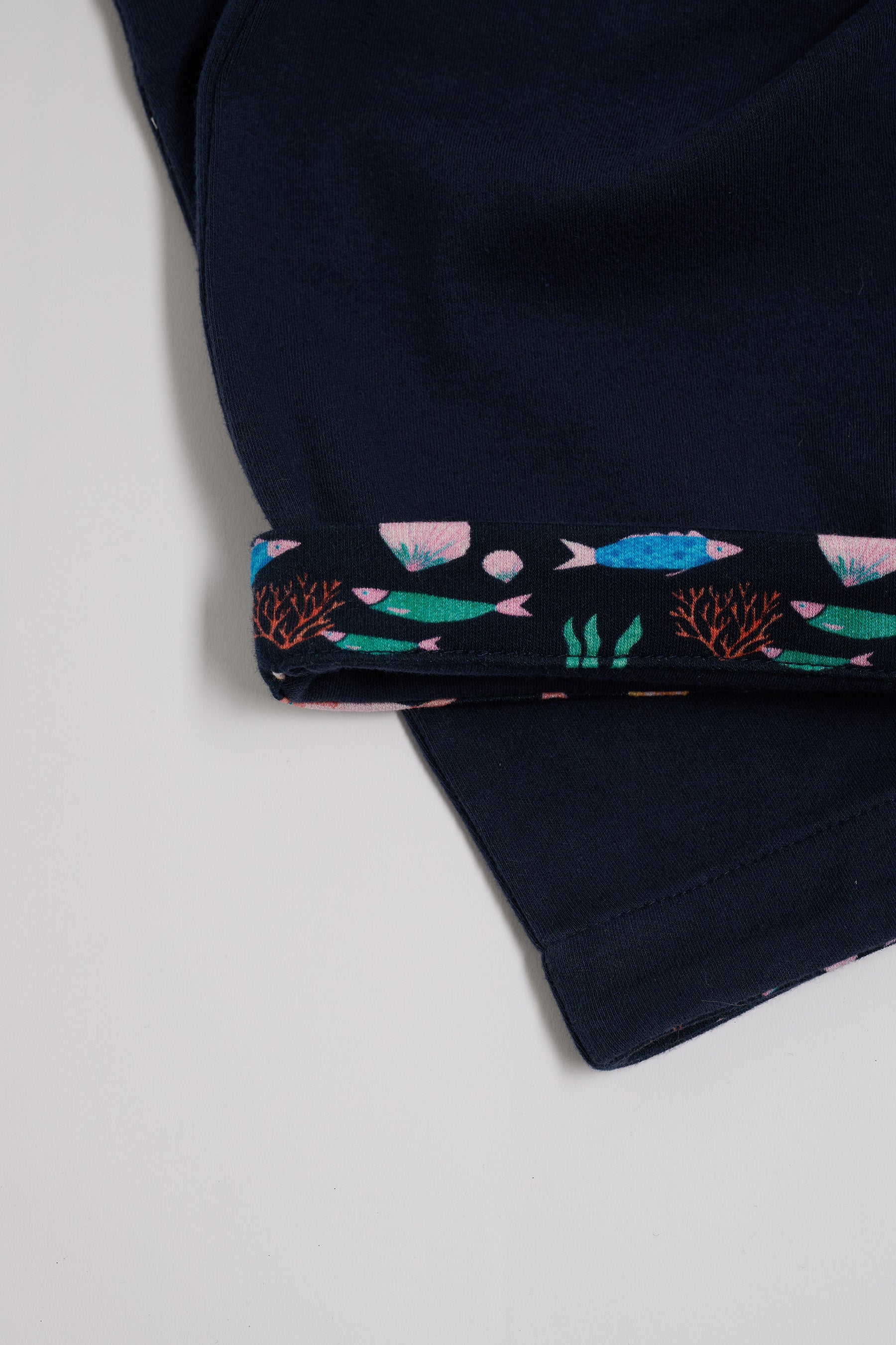 Close-up of vibrant fish print turn-up on navy short dungarees.