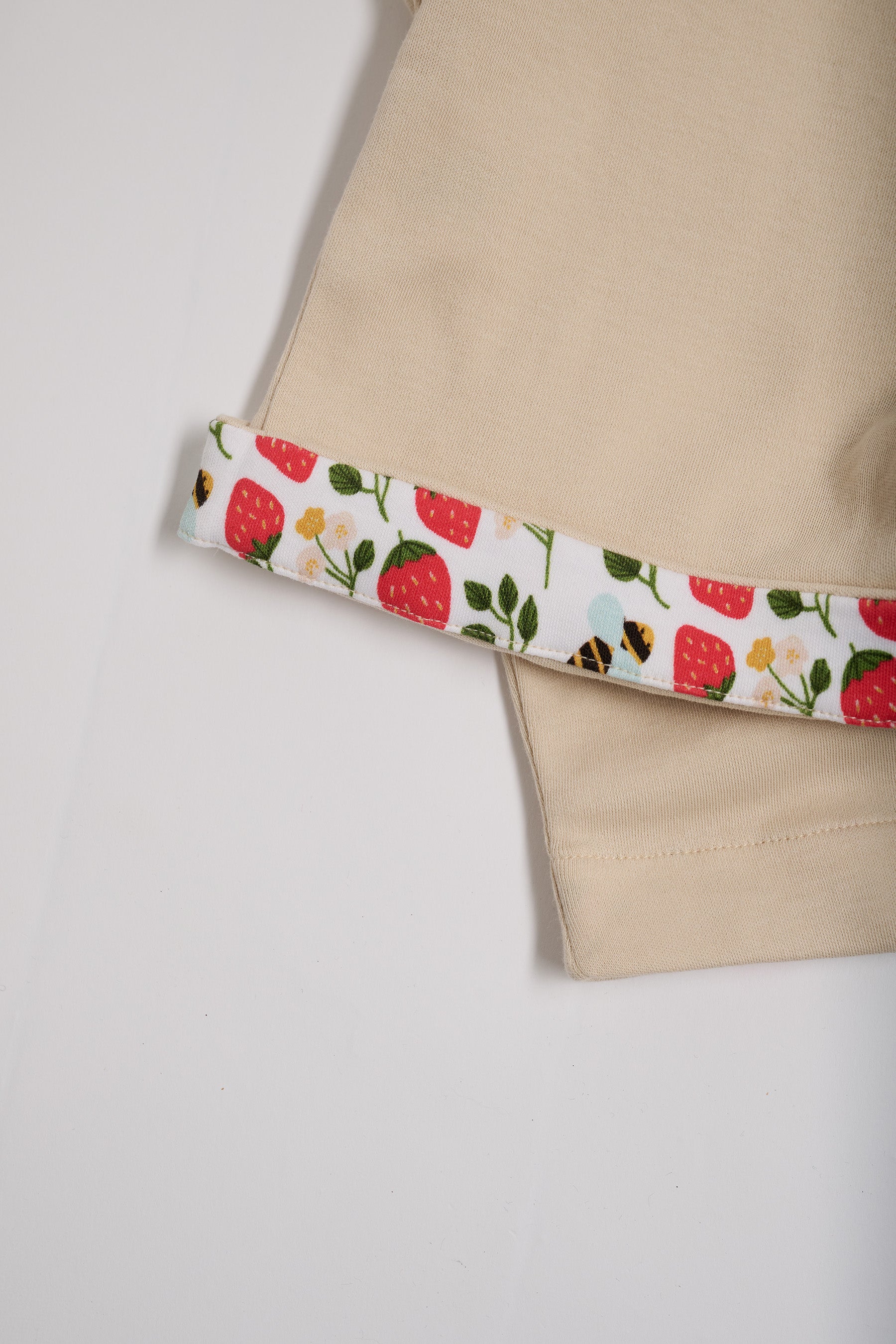 Close-up of strawberry and bees print turn-up on beige short dungarees.