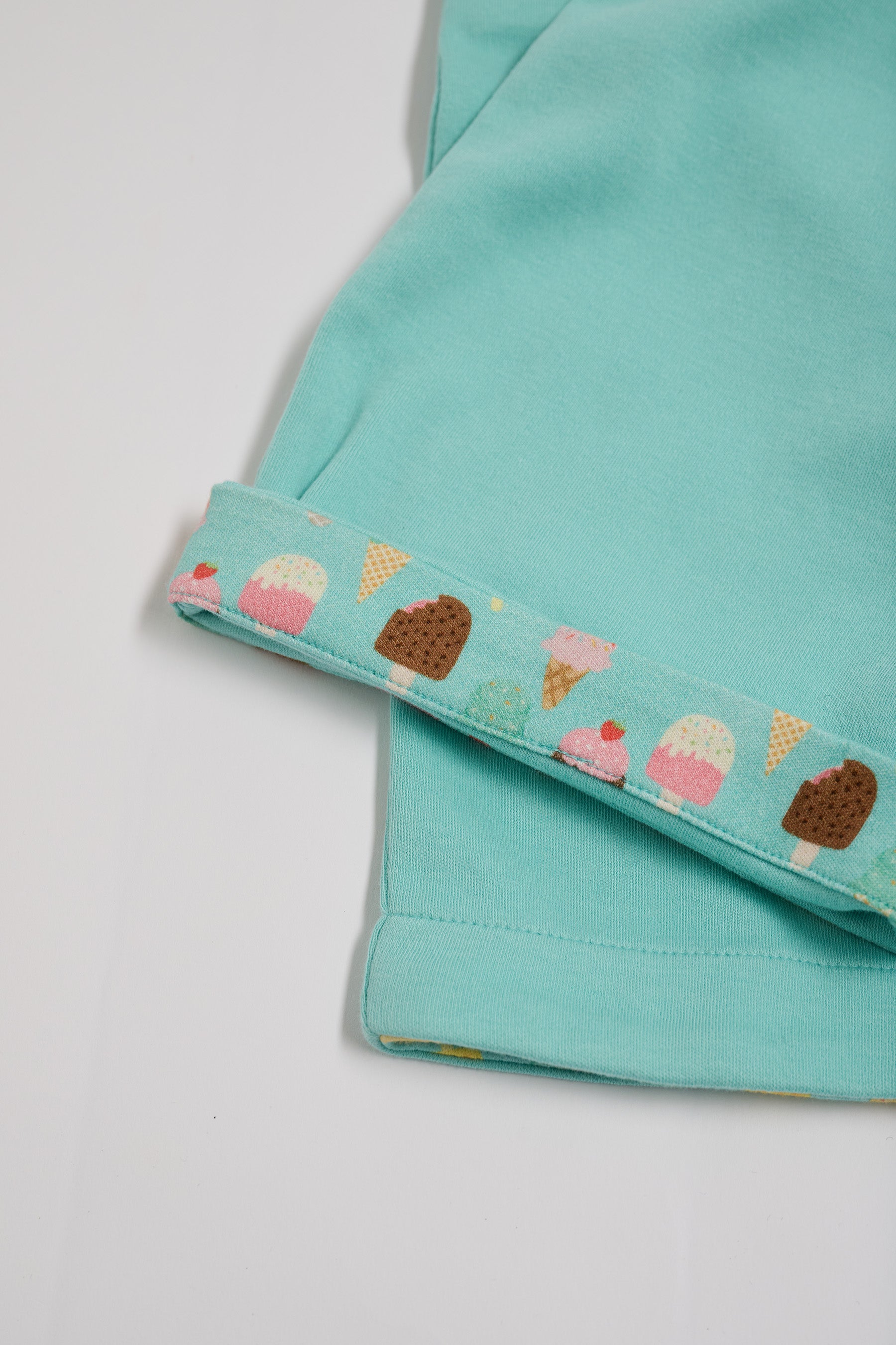 Close-up of bright ice cream print turn-ups on turquoise short dungarees.